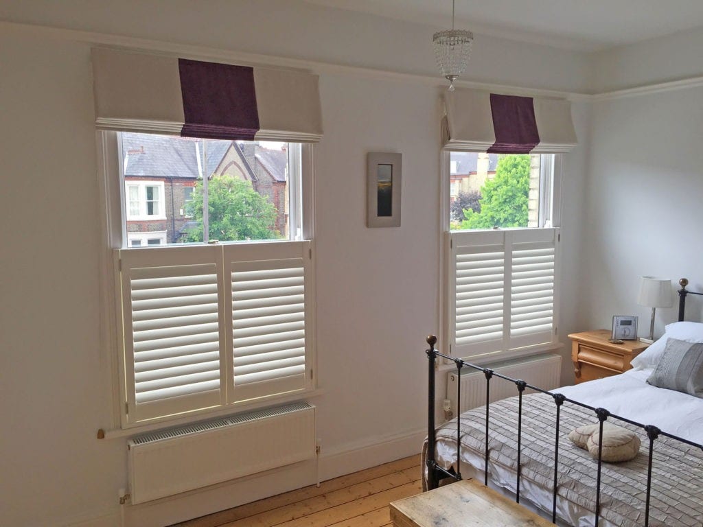 Café style shutters in a bedroom with a wrought iron bed
